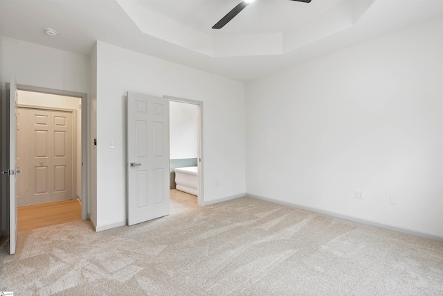 unfurnished bedroom with light carpet, a tray ceiling, ceiling fan, and ensuite bathroom