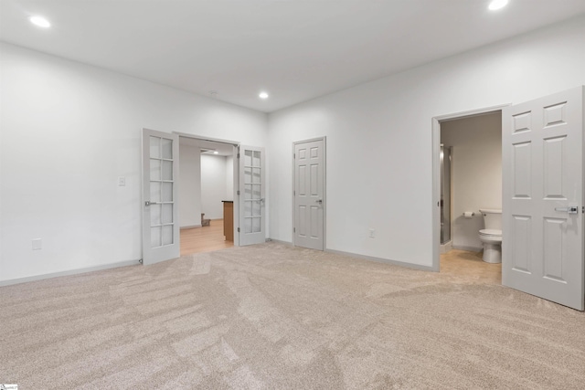 unfurnished bedroom featuring connected bathroom, light colored carpet, and french doors