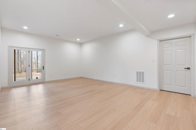 empty room with light hardwood / wood-style flooring and beamed ceiling