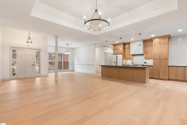 kitchen with ornate columns, pendant lighting, an island with sink, white fridge with ice dispenser, and a tray ceiling