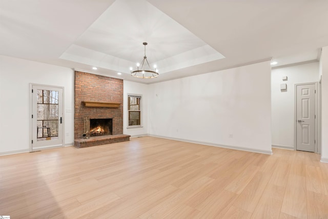 unfurnished living room featuring a fireplace, a tray ceiling, and light wood-type flooring