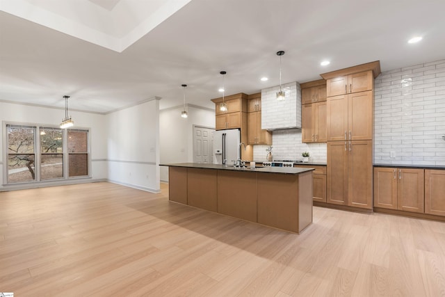 kitchen with pendant lighting, high end fridge, a kitchen island with sink, tasteful backsplash, and light hardwood / wood-style floors