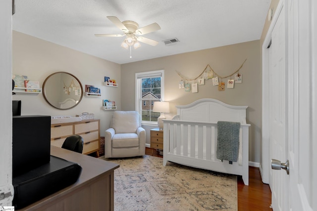 bedroom featuring a nursery area, ceiling fan, hardwood / wood-style floors, and a textured ceiling