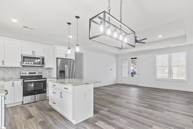 kitchen featuring white cabinetry, stainless steel appliances, a center island, decorative light fixtures, and a raised ceiling