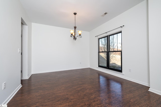 empty room with a notable chandelier and dark hardwood / wood-style floors