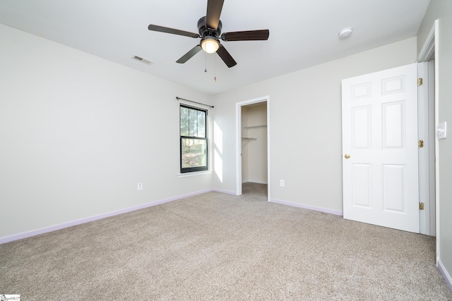 unfurnished bedroom featuring a spacious closet, carpet floors, a closet, and ceiling fan