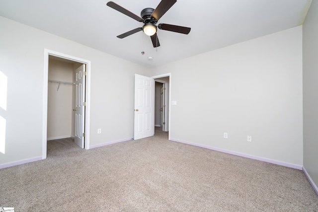 unfurnished bedroom with light carpet, a walk in closet, a closet, and ceiling fan