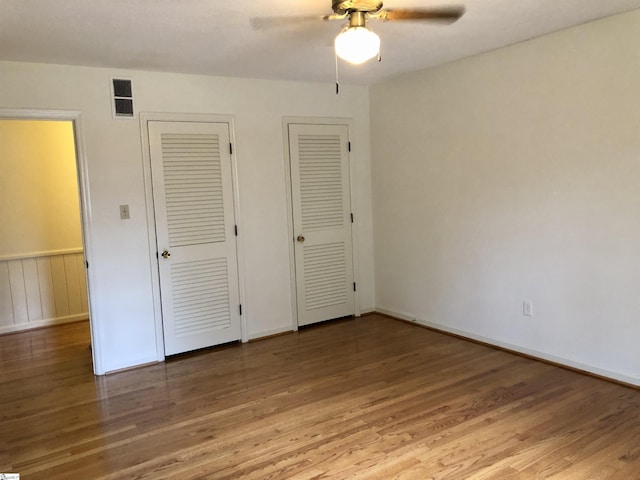 unfurnished bedroom featuring multiple closets, hardwood / wood-style flooring, and ceiling fan