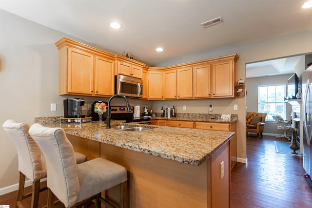 kitchen with dark wood-type flooring, a breakfast bar area, light stone counters, kitchen peninsula, and stainless steel appliances