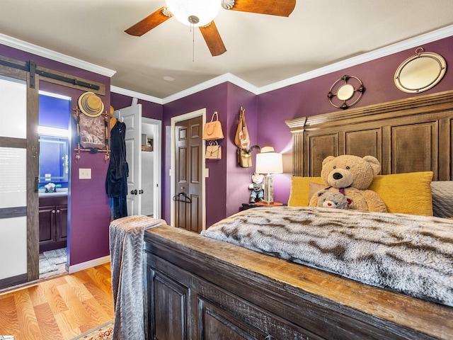 bedroom featuring ensuite bath, ceiling fan, ornamental molding, light hardwood / wood-style floors, and a barn door