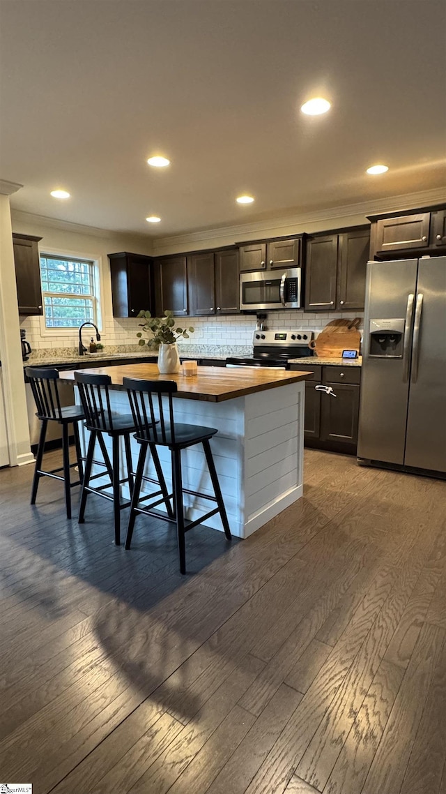 kitchen with dark wood-type flooring, a breakfast bar area, dark brown cabinets, appliances with stainless steel finishes, and decorative backsplash