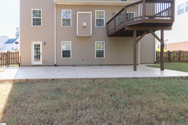 back of house featuring a wooden deck, a patio, and a lawn