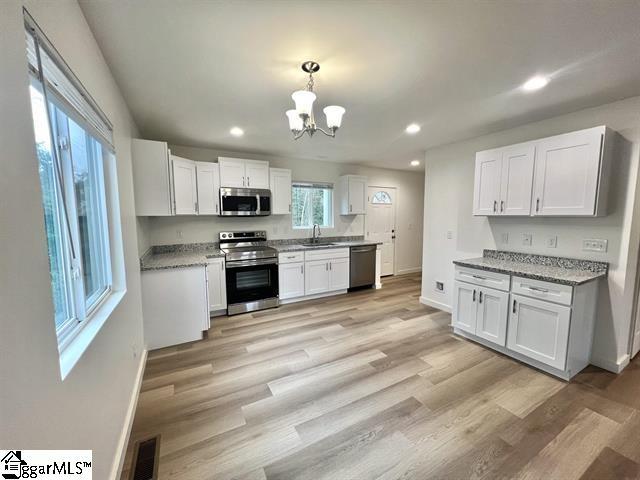 kitchen with white cabinetry, light stone counters, hanging light fixtures, stainless steel appliances, and light hardwood / wood-style floors