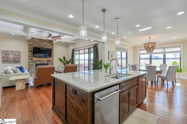 kitchen with a stone fireplace, sink, dishwasher, light stone countertops, and a kitchen island with sink