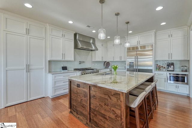 kitchen featuring pendant lighting, white cabinets, appliances with stainless steel finishes, and wall chimney range hood