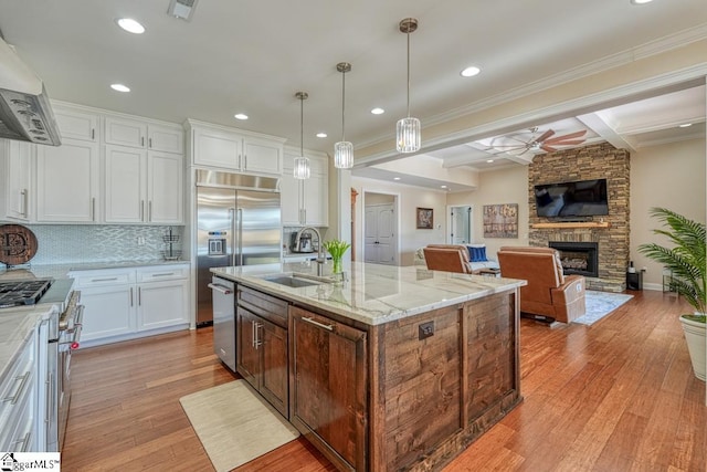 kitchen with premium appliances, an island with sink, white cabinets, a fireplace, and exhaust hood