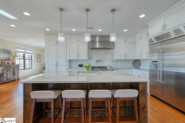 kitchen featuring a center island with sink, wall chimney exhaust hood, and built in refrigerator