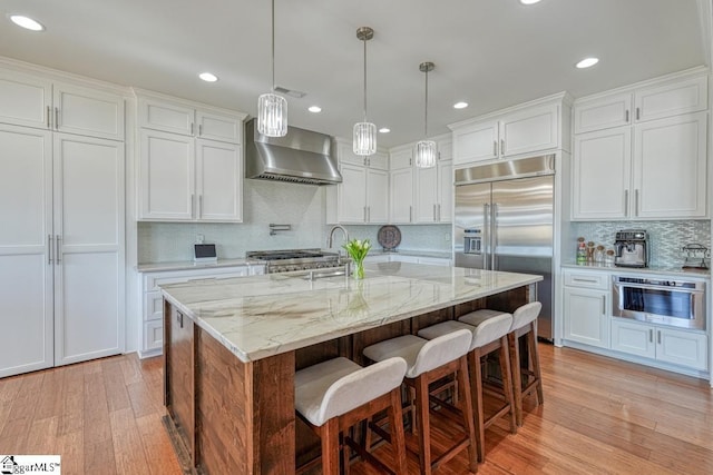 kitchen with white cabinetry, appliances with stainless steel finishes, wall chimney exhaust hood, and a center island with sink