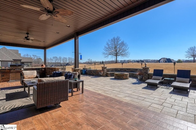 view of patio / terrace featuring a grill, an outdoor living space with a fire pit, ceiling fan, and exterior kitchen