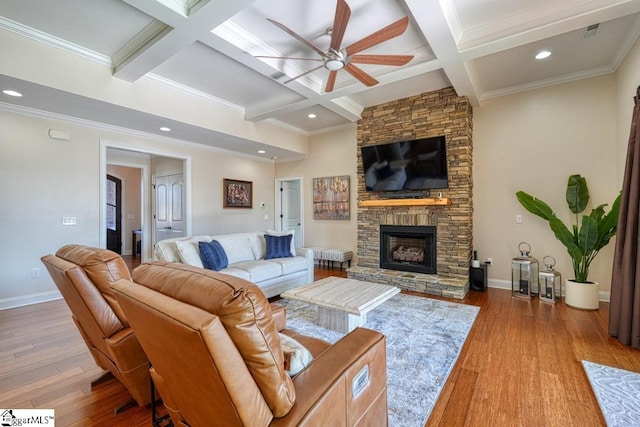 living room featuring ceiling fan, beam ceiling, coffered ceiling, wood-type flooring, and a stone fireplace