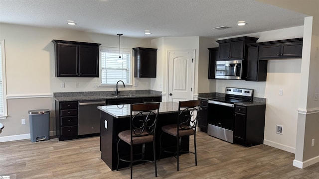 kitchen featuring a kitchen island, stone countertops, sink, stainless steel appliances, and light hardwood / wood-style flooring