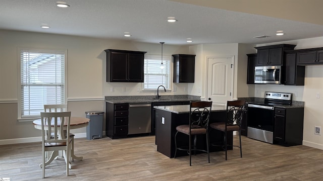 kitchen with sink, stainless steel appliances, a kitchen breakfast bar, a kitchen island, and light wood-type flooring