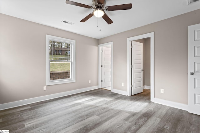 unfurnished bedroom featuring a spacious closet, dark wood-type flooring, and ceiling fan