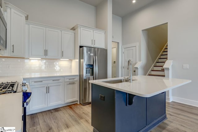 kitchen featuring an island with sink, sink, white cabinets, stainless steel appliances, and light wood-type flooring