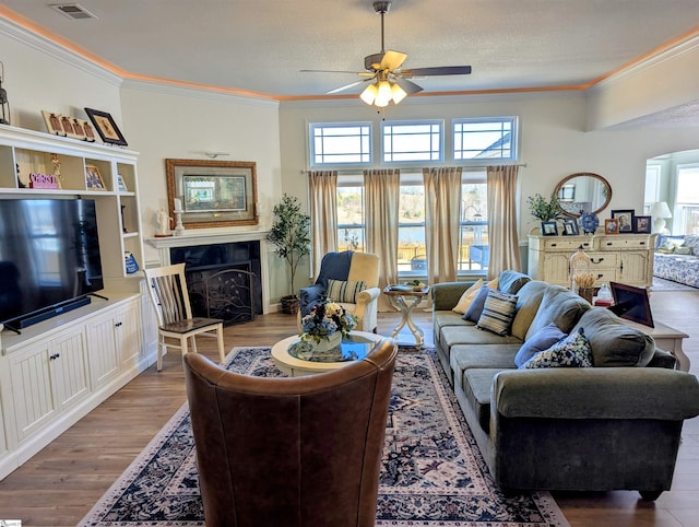 living room with crown molding, ceiling fan, wood-type flooring, and a textured ceiling