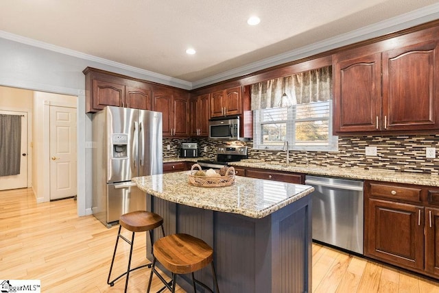 kitchen featuring a breakfast bar area, stainless steel appliances, light stone countertops, a kitchen island, and light wood-type flooring