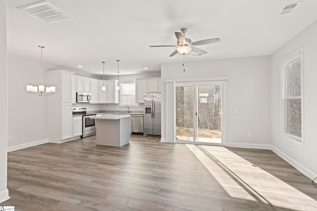 kitchen featuring white cabinets, hanging light fixtures, a center island, stainless steel appliances, and light hardwood / wood-style flooring