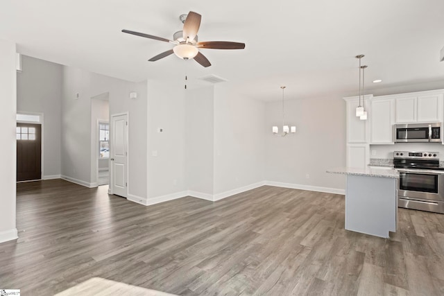 kitchen with white cabinetry, light stone counters, pendant lighting, stainless steel appliances, and hardwood / wood-style floors