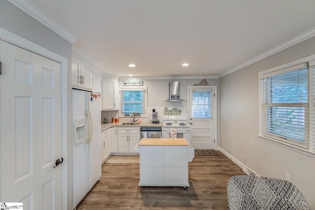 kitchen with sink, white cabinets, ornamental molding, wall chimney range hood, and white appliances