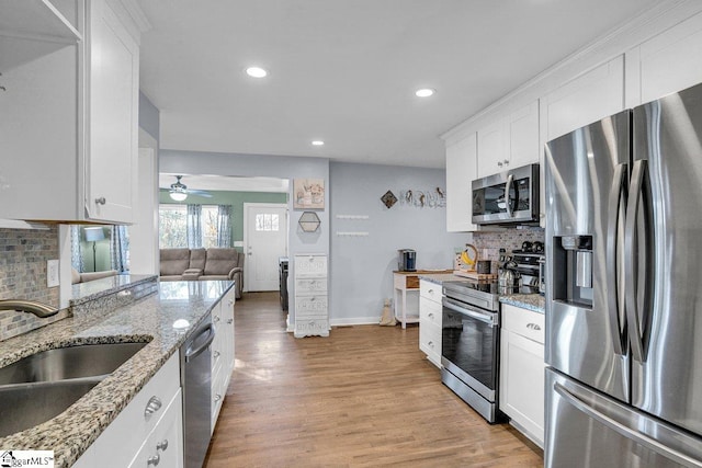 kitchen with sink, white cabinets, light stone counters, stainless steel appliances, and light hardwood / wood-style flooring