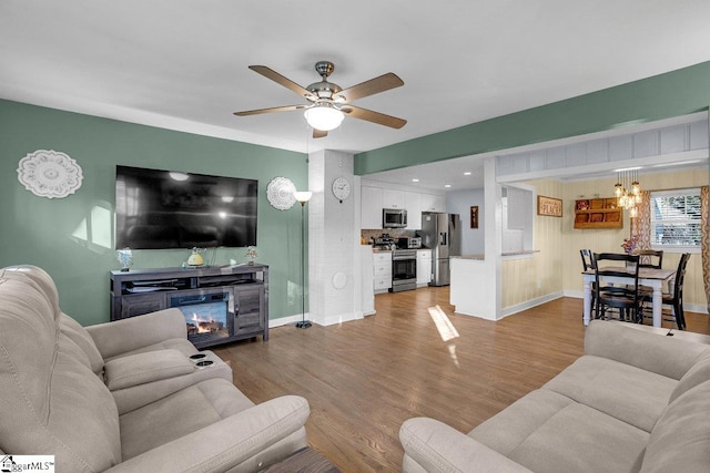 living room with ceiling fan with notable chandelier and light hardwood / wood-style floors