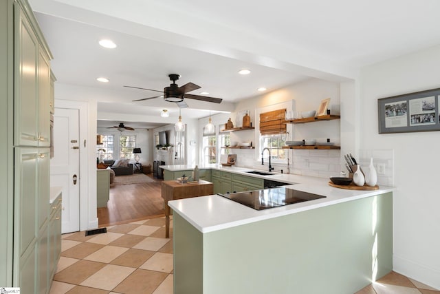 kitchen featuring sink, green cabinetry, black electric cooktop, decorative backsplash, and kitchen peninsula