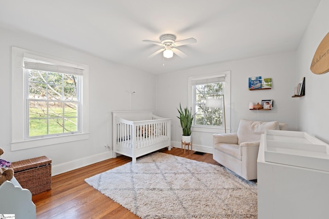 bedroom featuring hardwood / wood-style floors, a crib, and ceiling fan