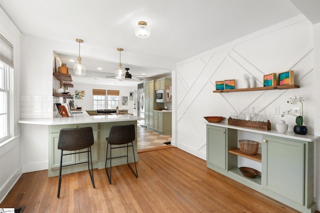 kitchen featuring a kitchen bar, light hardwood / wood-style flooring, kitchen peninsula, and green cabinets