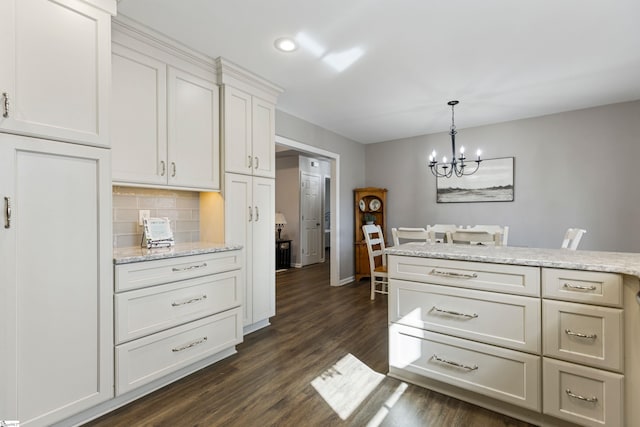 kitchen featuring tasteful backsplash, white cabinets, dark hardwood / wood-style flooring, a chandelier, and light stone counters