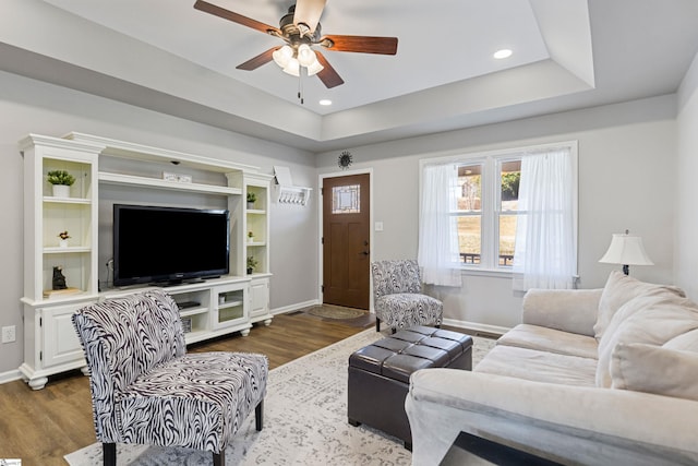 living room with dark wood-type flooring, ceiling fan, and a tray ceiling