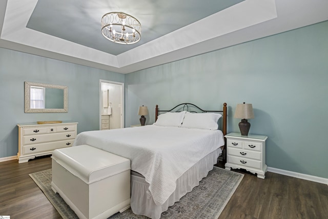 bedroom featuring a raised ceiling, dark hardwood / wood-style floors, connected bathroom, and an inviting chandelier