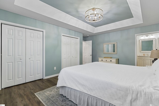 bedroom featuring connected bathroom, two closets, dark hardwood / wood-style flooring, a notable chandelier, and a raised ceiling