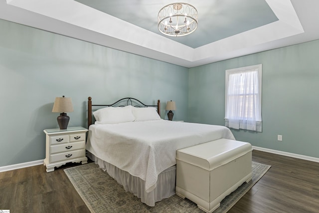 bedroom featuring dark wood-type flooring, a tray ceiling, and a chandelier