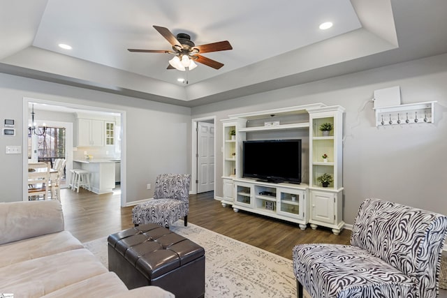 living room with ceiling fan with notable chandelier, dark hardwood / wood-style flooring, and a tray ceiling