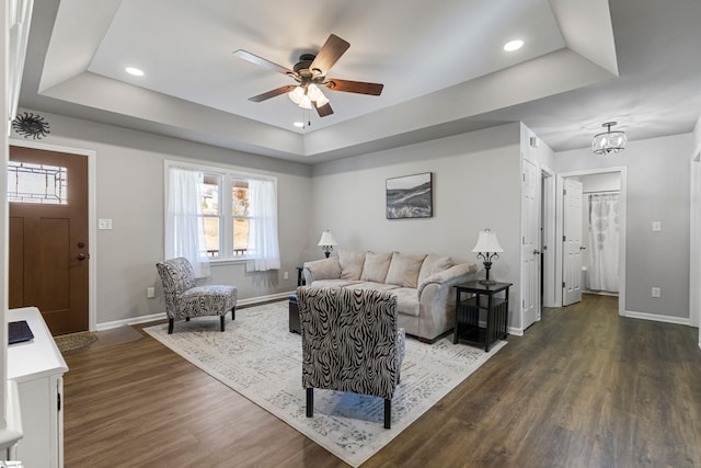 living room with dark hardwood / wood-style flooring, a raised ceiling, and ceiling fan