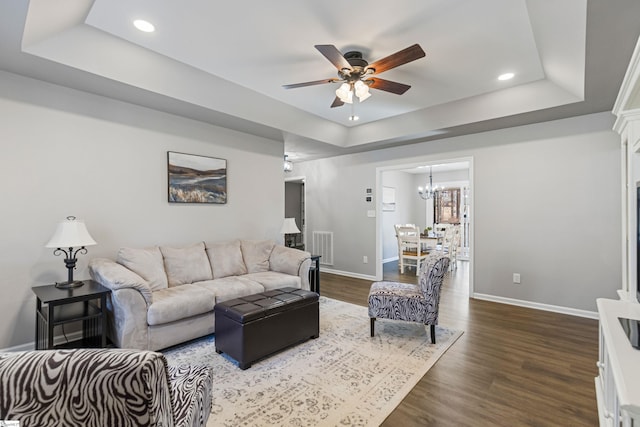 living room featuring dark hardwood / wood-style floors, ceiling fan with notable chandelier, and a raised ceiling