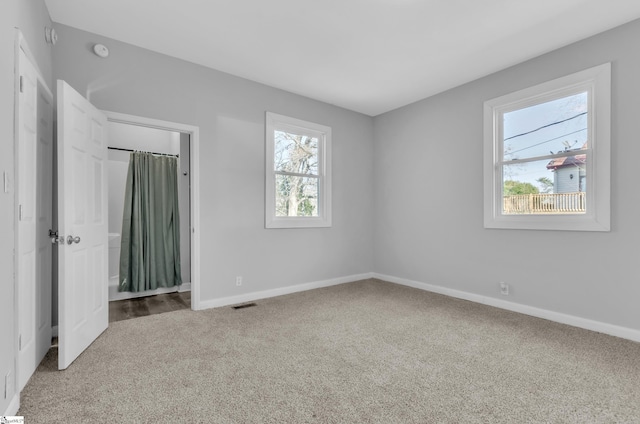 unfurnished bedroom featuring multiple windows, carpet floors, and connected bathroom