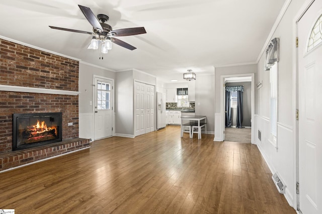 unfurnished living room with hardwood / wood-style flooring, ceiling fan, crown molding, and a brick fireplace