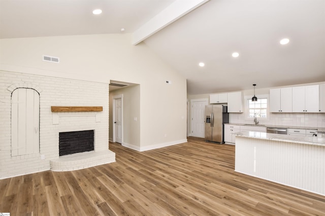 kitchen with hanging light fixtures, vaulted ceiling with beams, stainless steel appliances, light hardwood / wood-style floors, and white cabinets