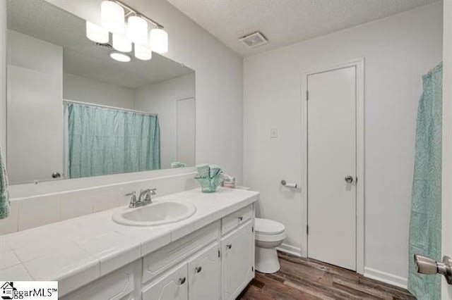 bathroom with an inviting chandelier, vanity, wood-type flooring, a textured ceiling, and toilet